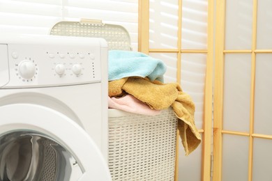 Photo of Wicker basket full of laundry and washing machine in bathroom