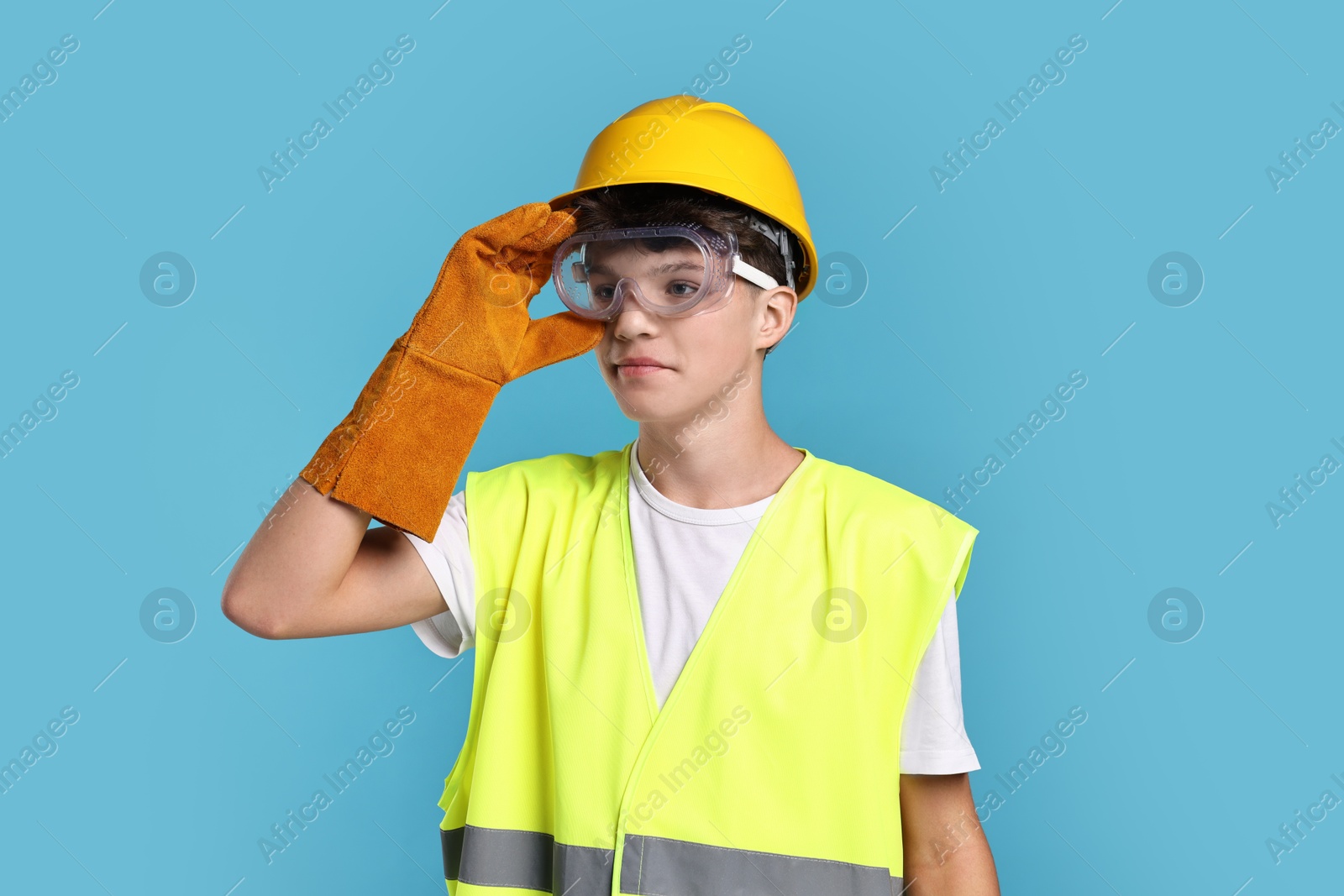 Photo of Teenage boy in hardhat, protective mask and safety vest working as builder on blue background