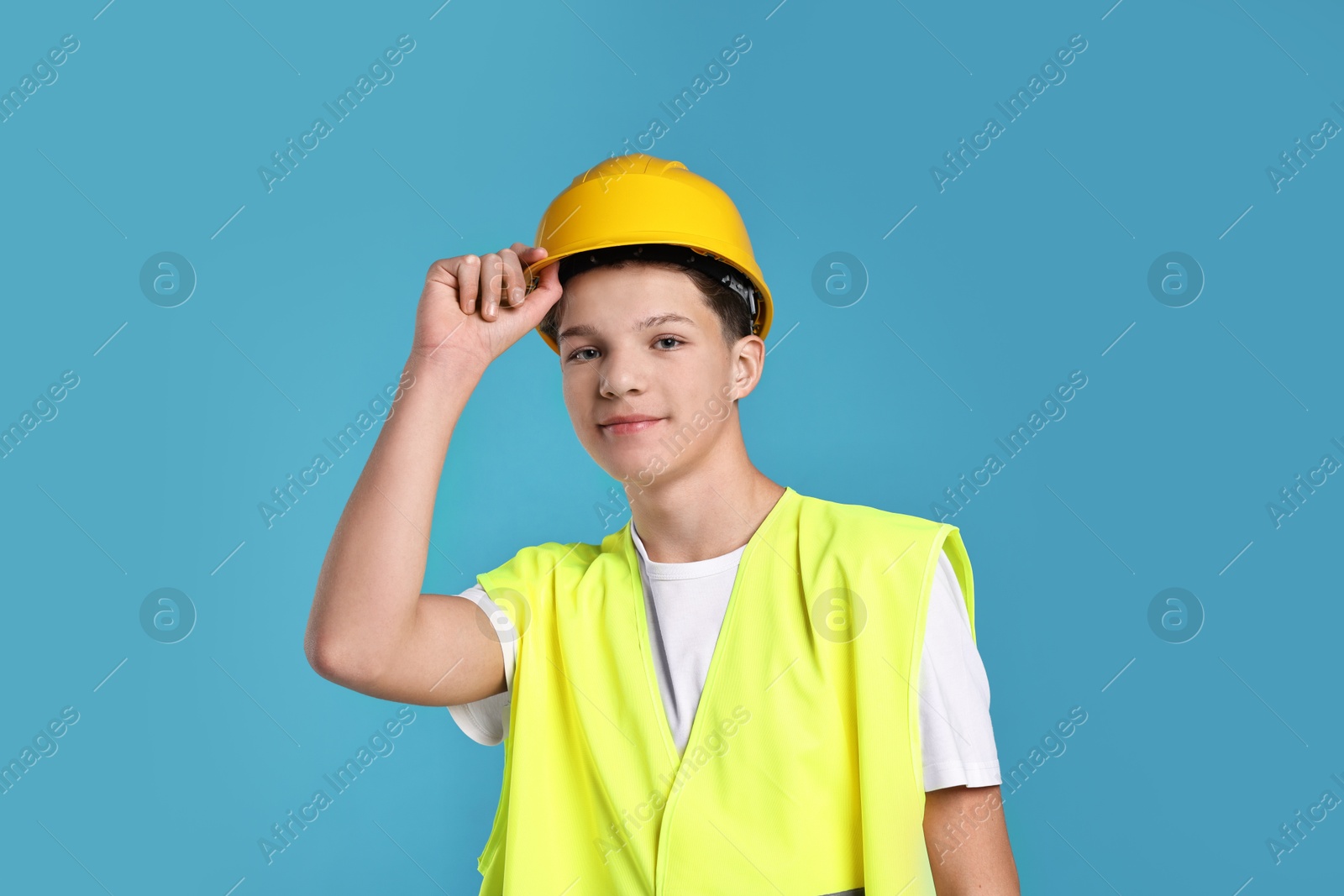 Photo of Teenage boy in hardhat and safety vest working as builder on blue background