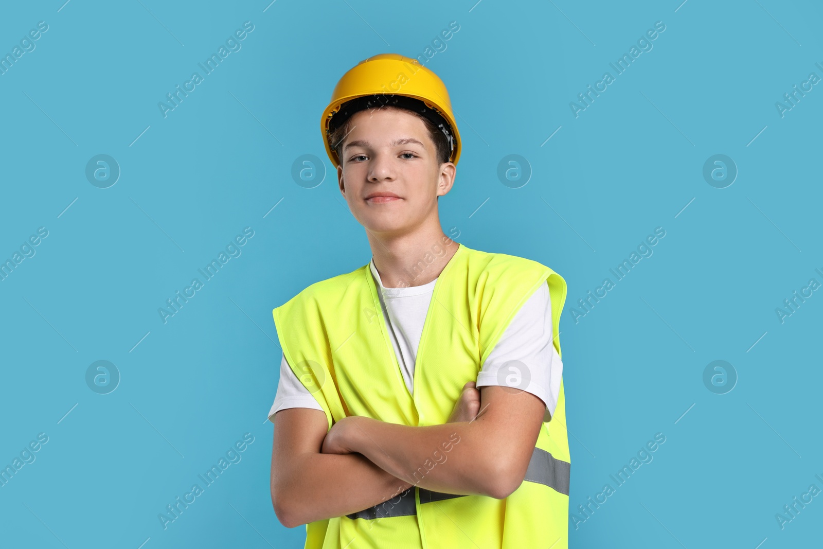 Photo of Teenage boy in hardhat and safety vest working as builder on blue background