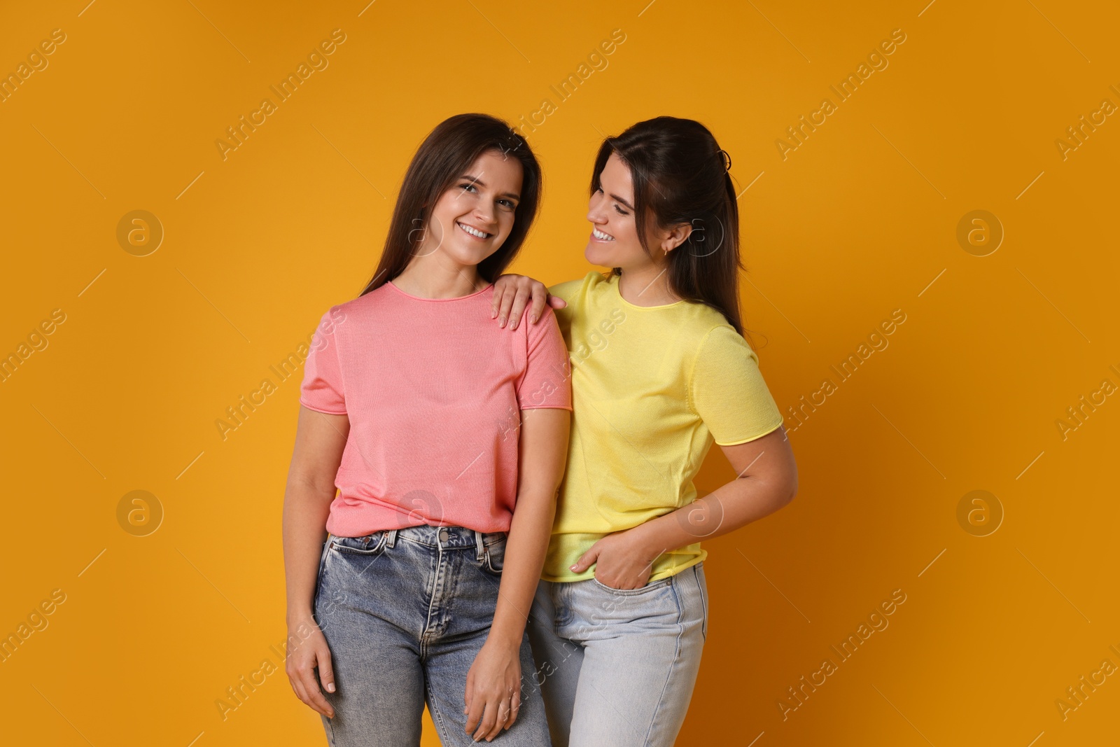 Photo of Portrait of happy twin sisters on orange background