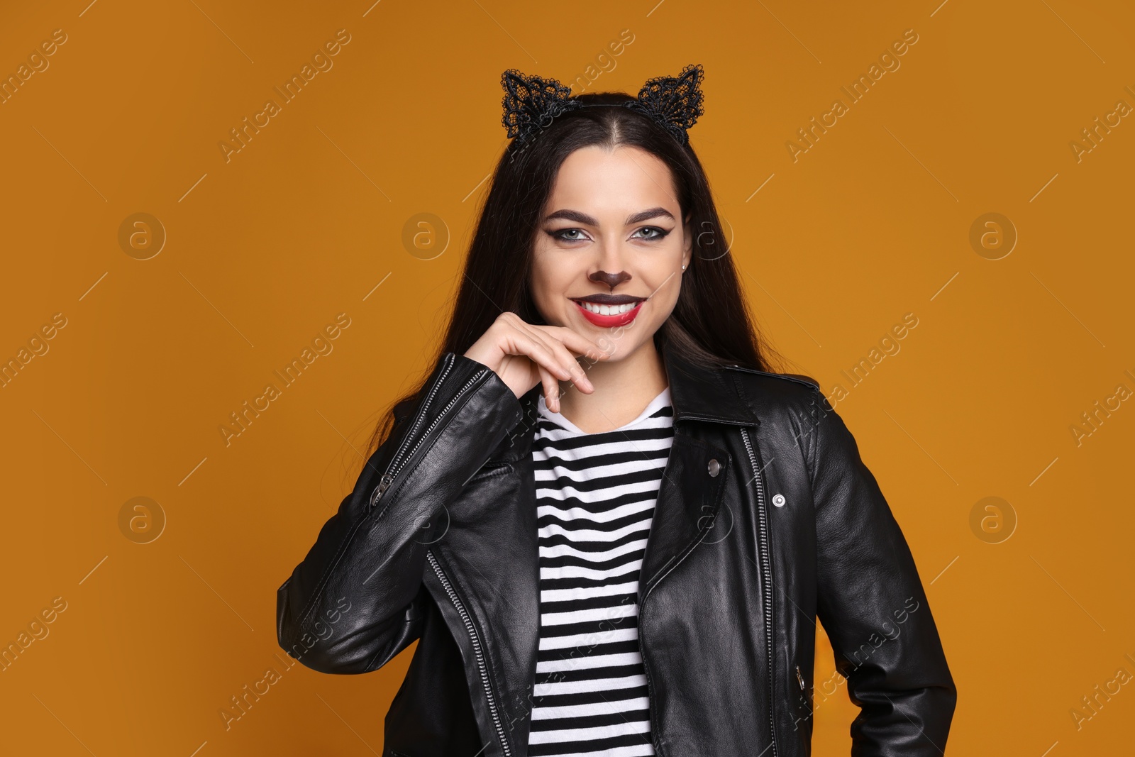 Photo of Woman with cat makeup and ears in leather jacket on orange background