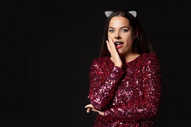 Photo of Emotional woman with cat makeup and ears on black background. Space for text