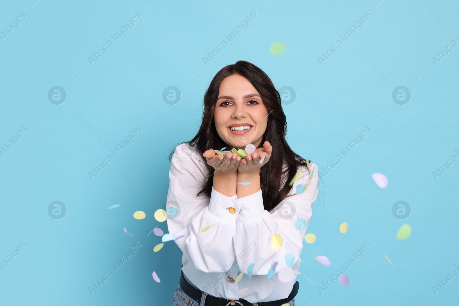 Photo of Happy woman with confetti on light blue background. Surprise party