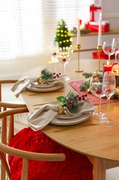 Photo of Christmas celebration. Festive table setting with dishware, glasses and decor in room