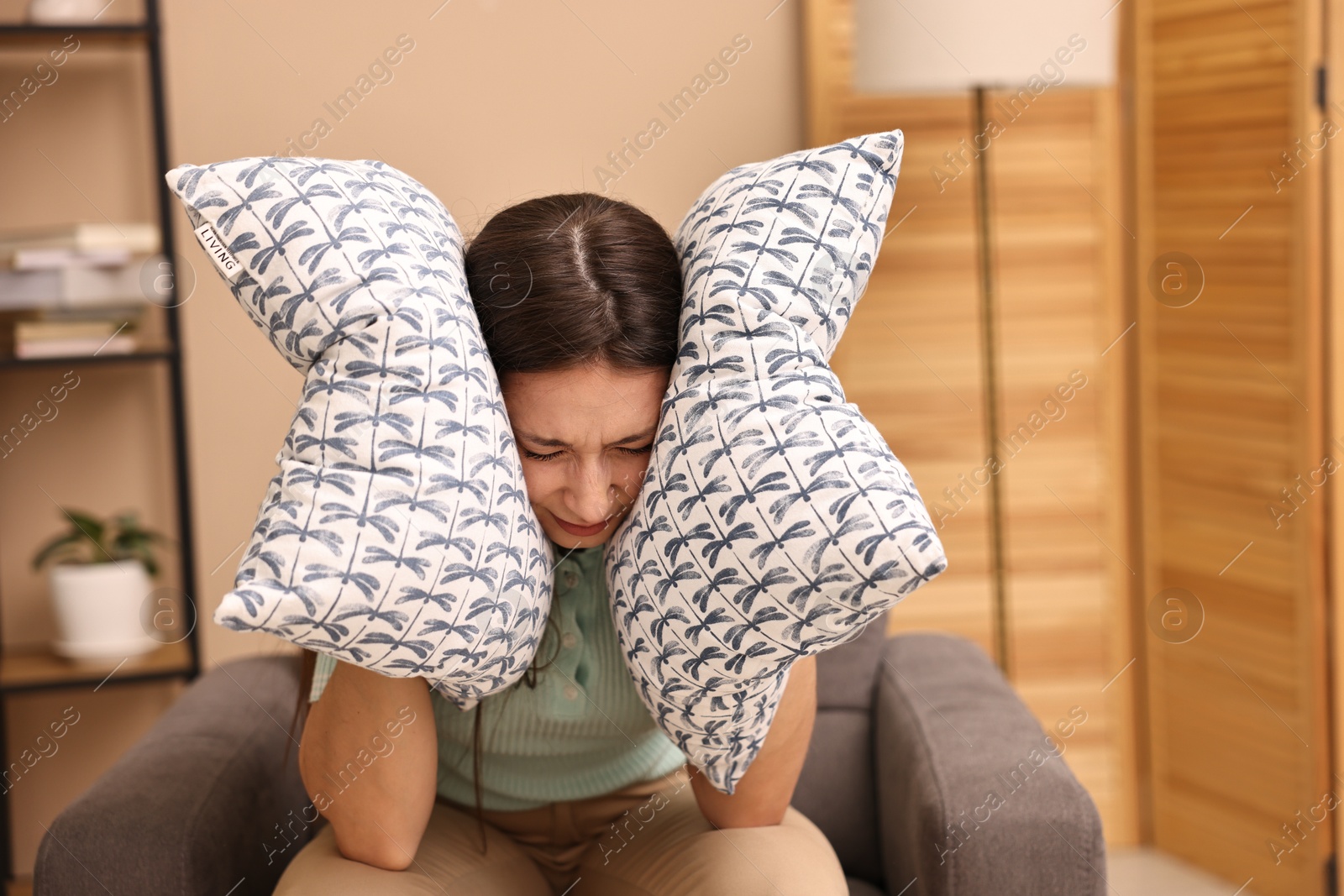 Photo of Annoyed woman covering her ears with pillows due to loud sound at home