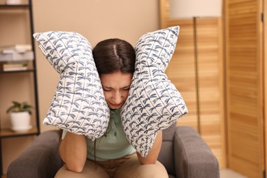 Annoyed woman covering her ears with pillows due to loud sound at home