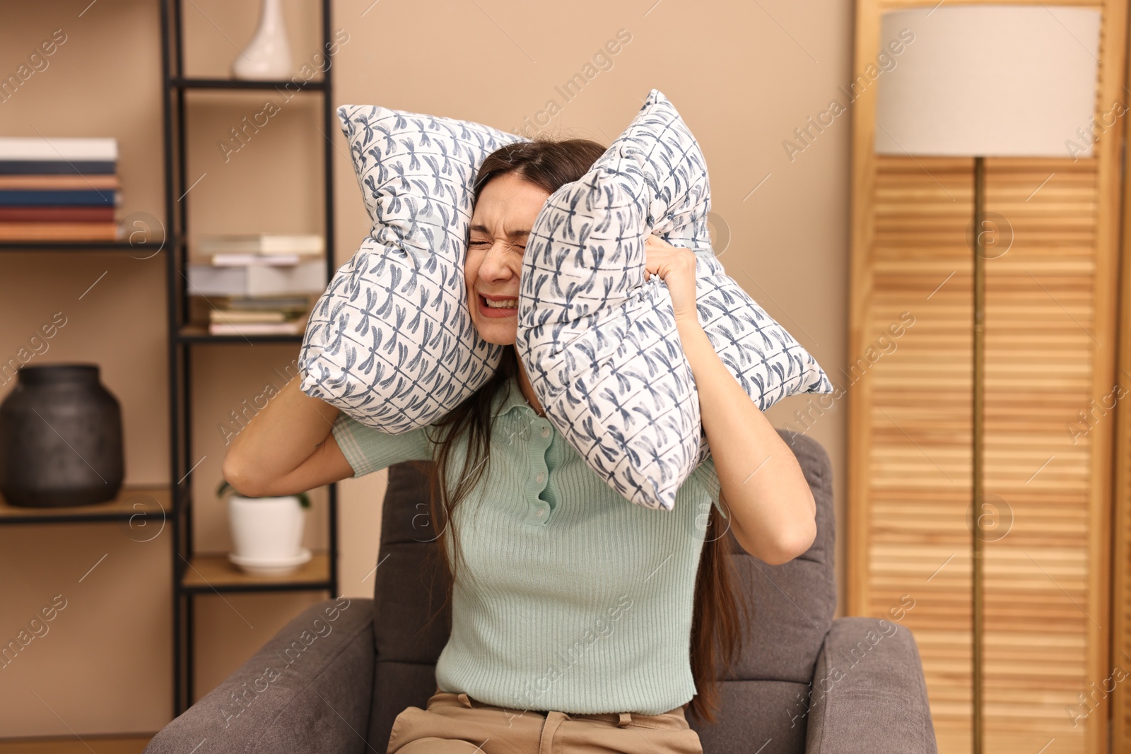 Photo of Annoyed woman covering her ears with pillows due to loud sound at home