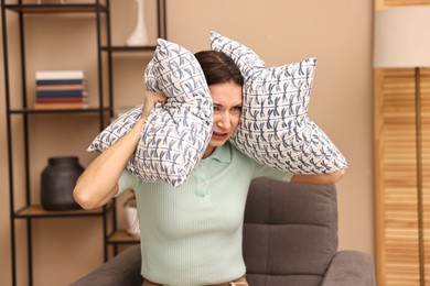 Photo of Annoyed woman covering her ears with pillows due to loud sound at home