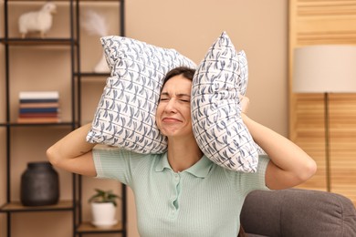 Photo of Annoyed woman covering her ears with pillows due to loud sound at home