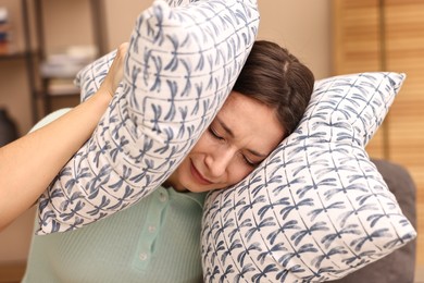 Photo of Annoyed woman covering her ears with pillows due to loud sound at home