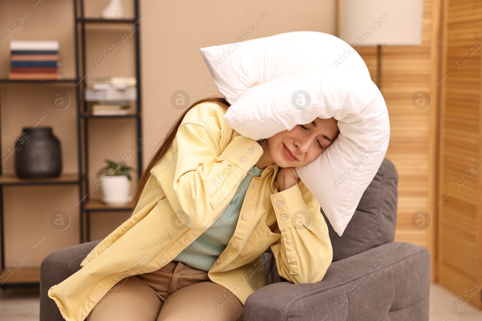 Photo of Annoyed woman covering her ears with pillow due to sound at home