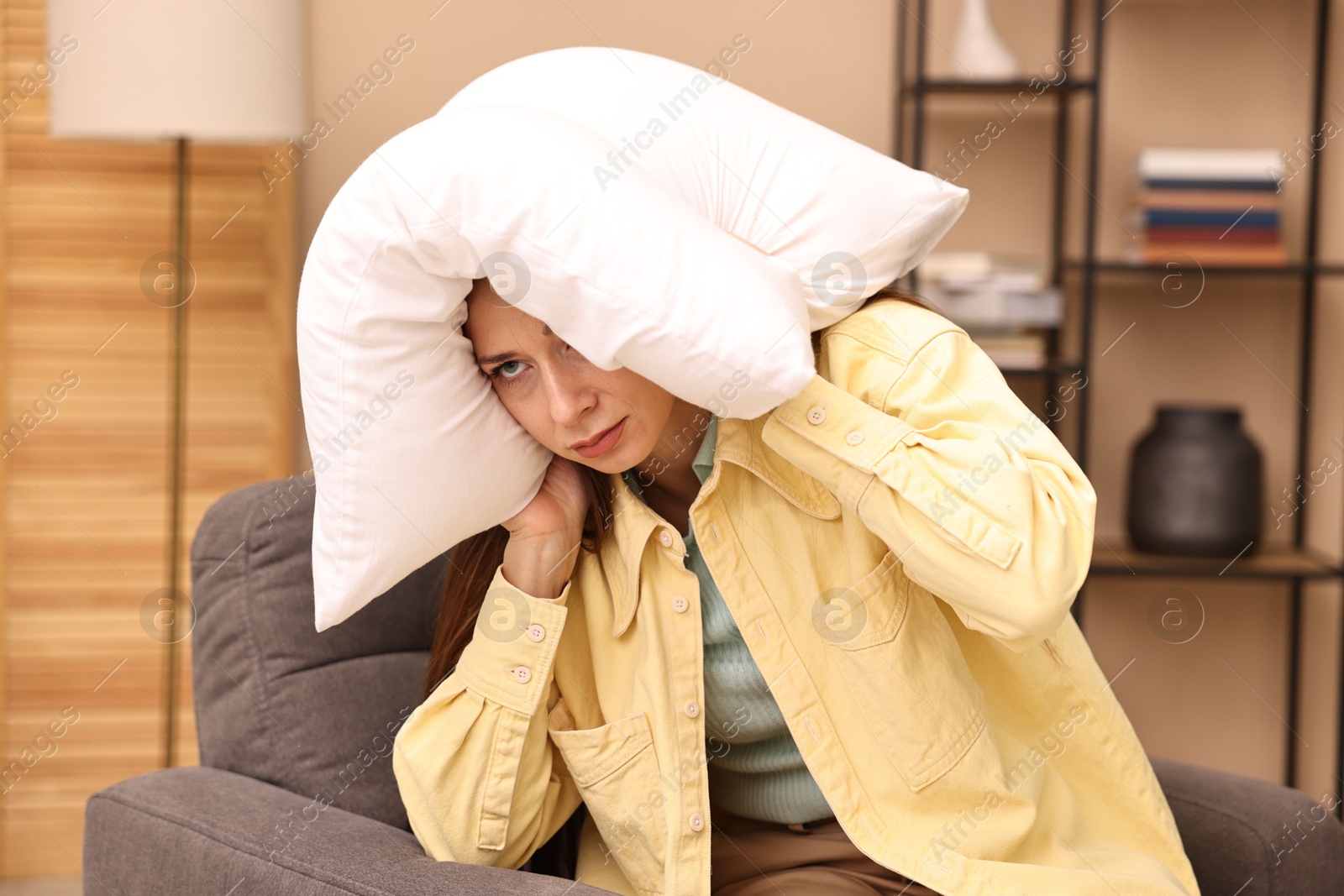 Photo of Annoyed woman covering her ears with pillow due to sound at home