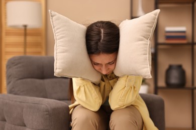 Photo of Annoyed woman covering her ears with pillows due to loud sound at home