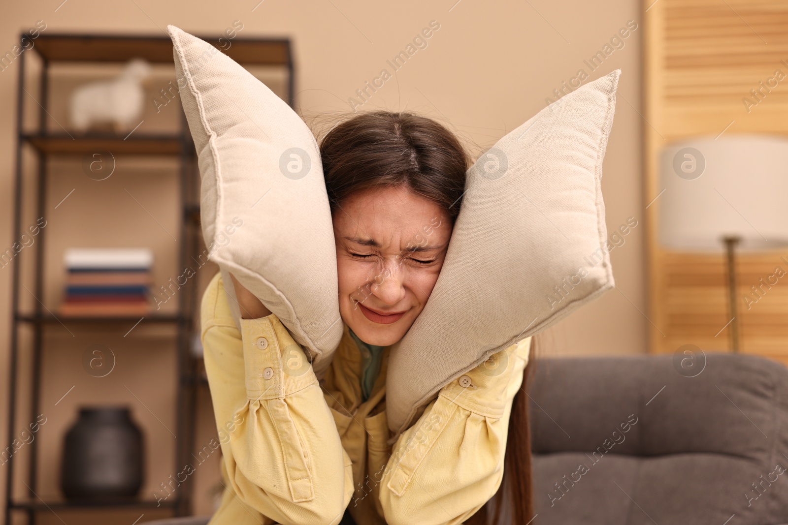 Photo of Annoyed woman covering her ears with pillows due to loud sound at home