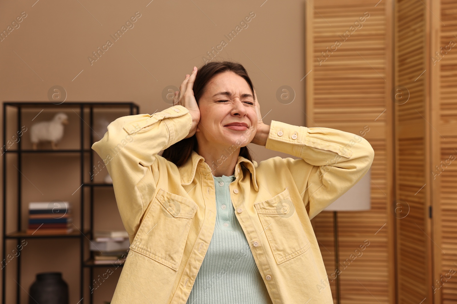 Photo of Annoyed woman covering her ears due to loud sound at home