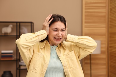 Annoyed woman covering her ears due to loud sound at home