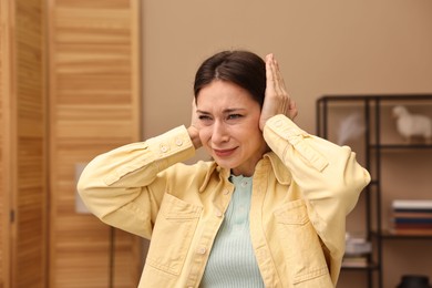 Annoyed woman covering her ears due to loud sound at home