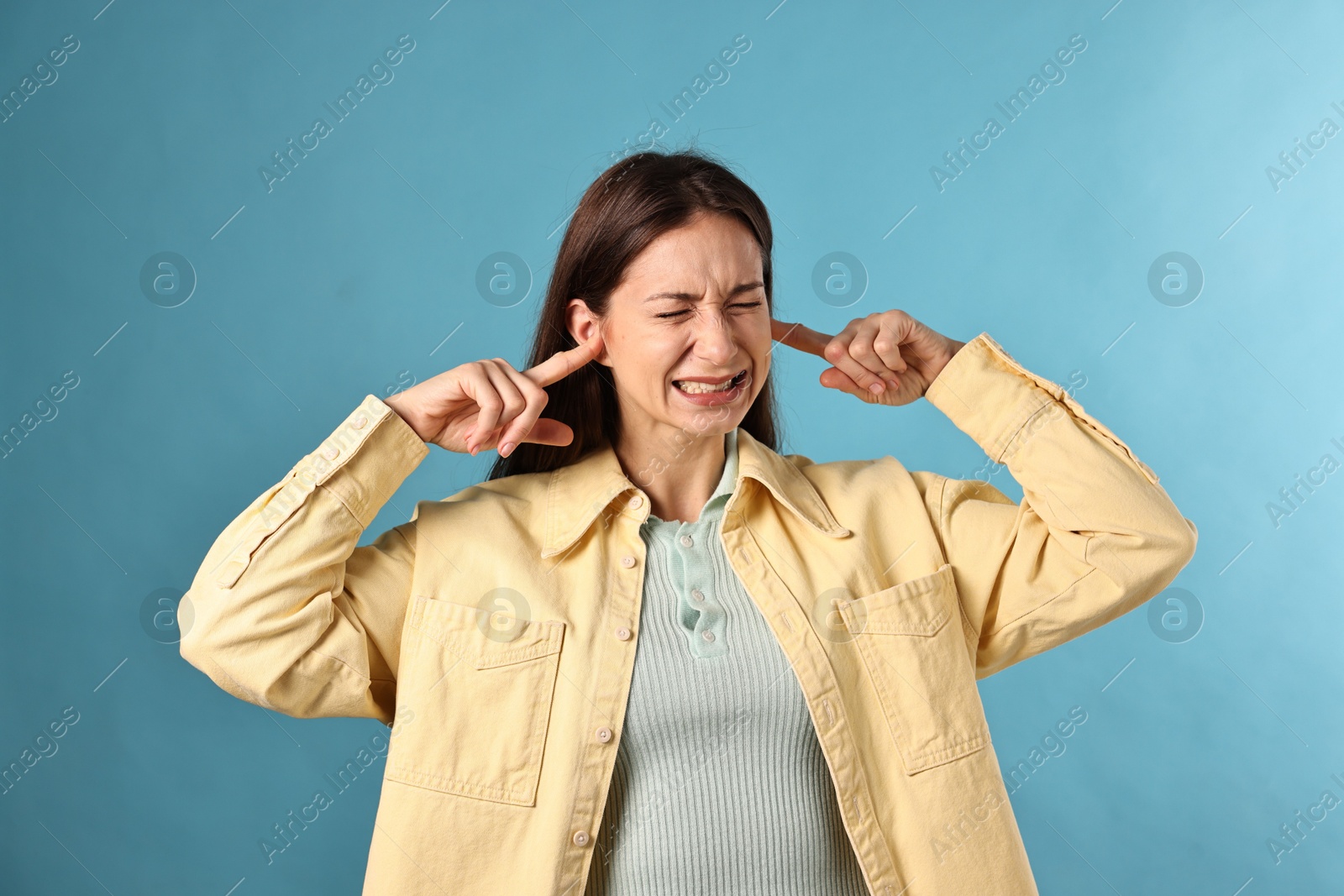 Photo of Annoyed woman covering her ears due to loud sound on light blue background