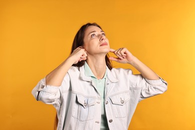 Annoyed woman covering her ears due to loud sound on orange background