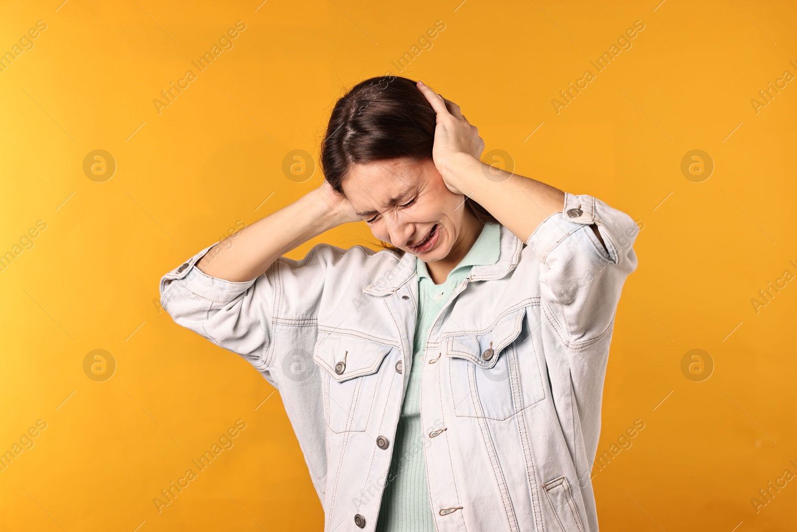 Photo of Annoyed woman covering her ears due to loud sound on orange background