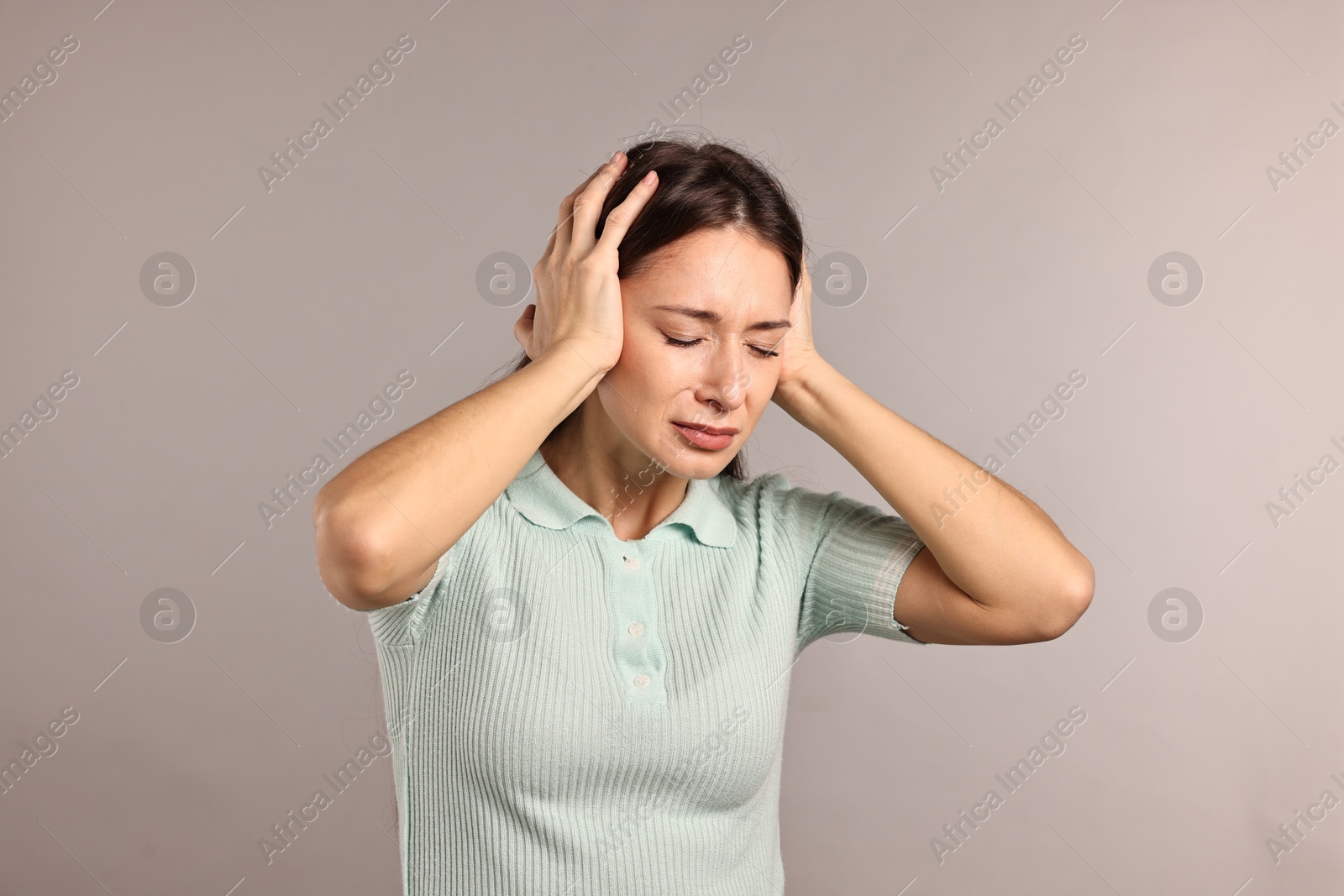 Photo of Annoyed woman covering her ears due to loud sound on light grey background