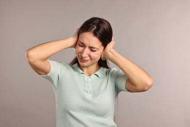 Photo of Annoyed woman covering her ears due to loud sound on light grey background