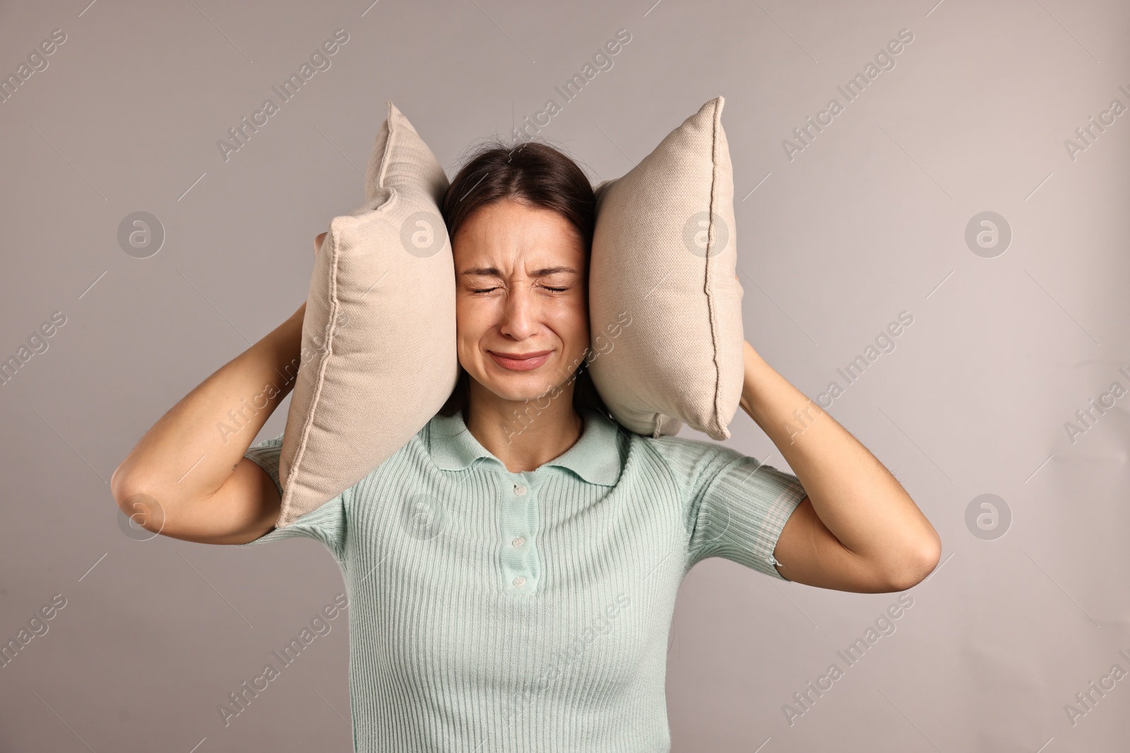 Photo of Annoyed woman covering her ears with pillows due to loud sound on light grey background