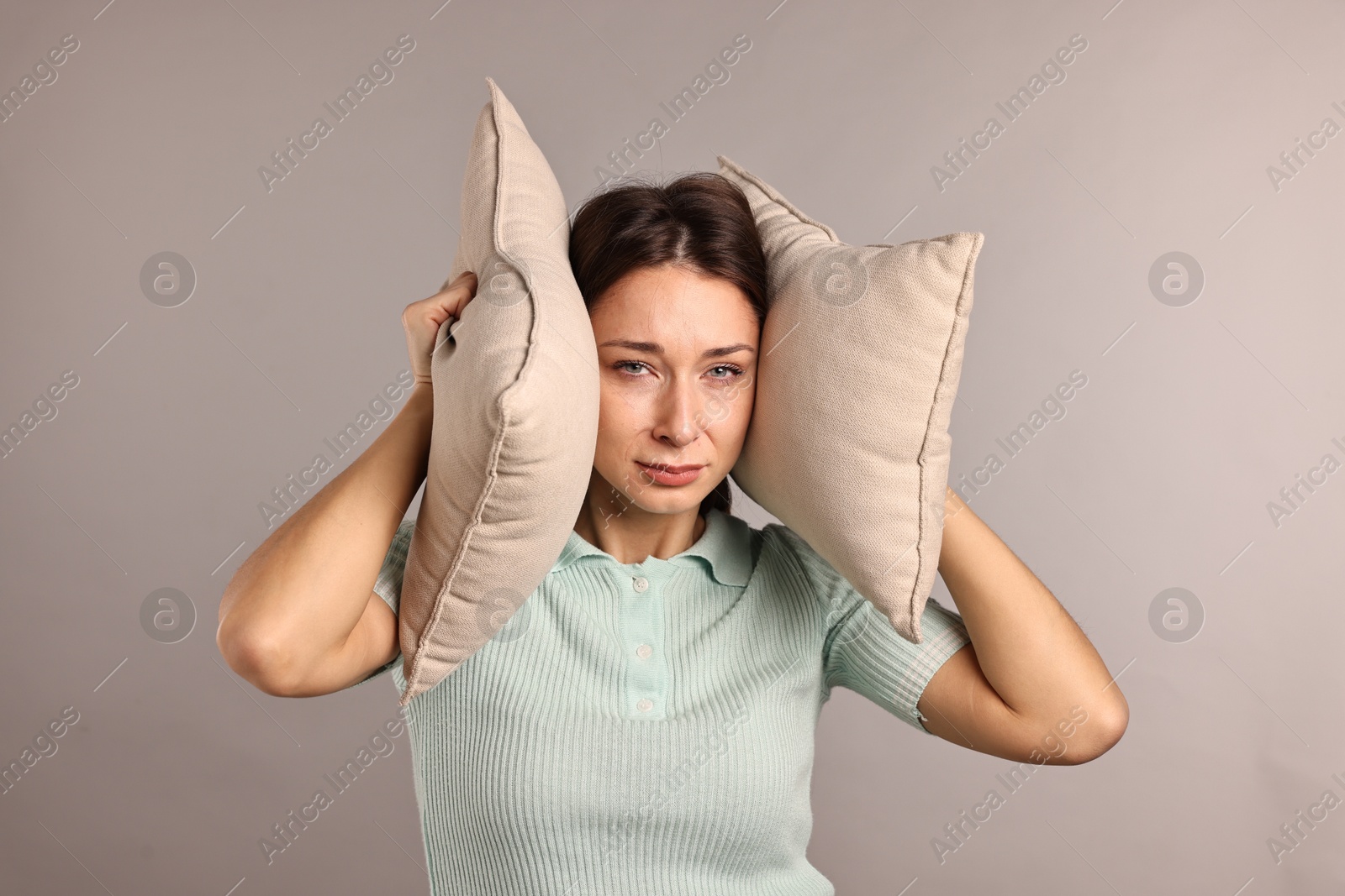 Photo of Annoyed woman covering her ears with pillows due to loud sound on light grey background