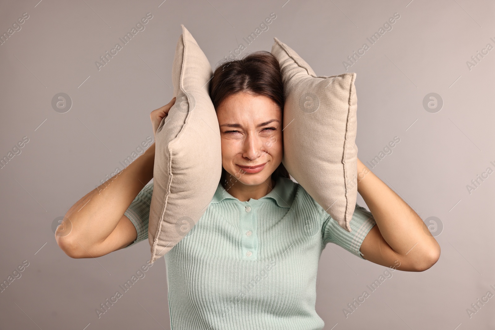 Photo of Annoyed woman covering her ears with pillows due to loud sound on light grey background