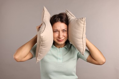 Photo of Annoyed woman covering her ears with pillows due to loud sound on light grey background