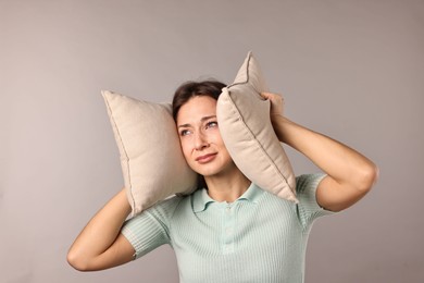 Photo of Annoyed woman covering her ears with pillows due to loud sound on light grey background