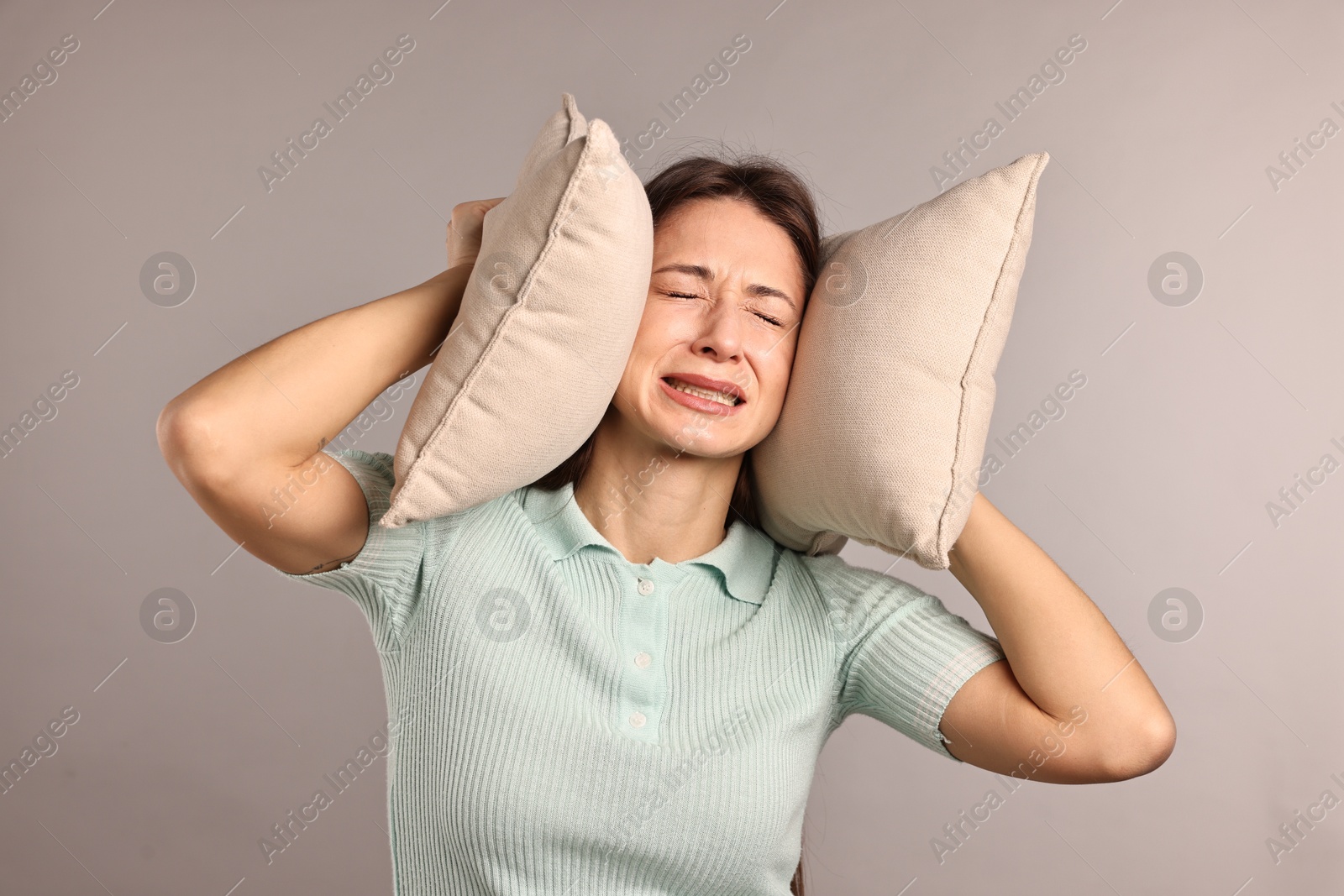 Photo of Annoyed woman covering her ears with pillows due to loud sound on light grey background