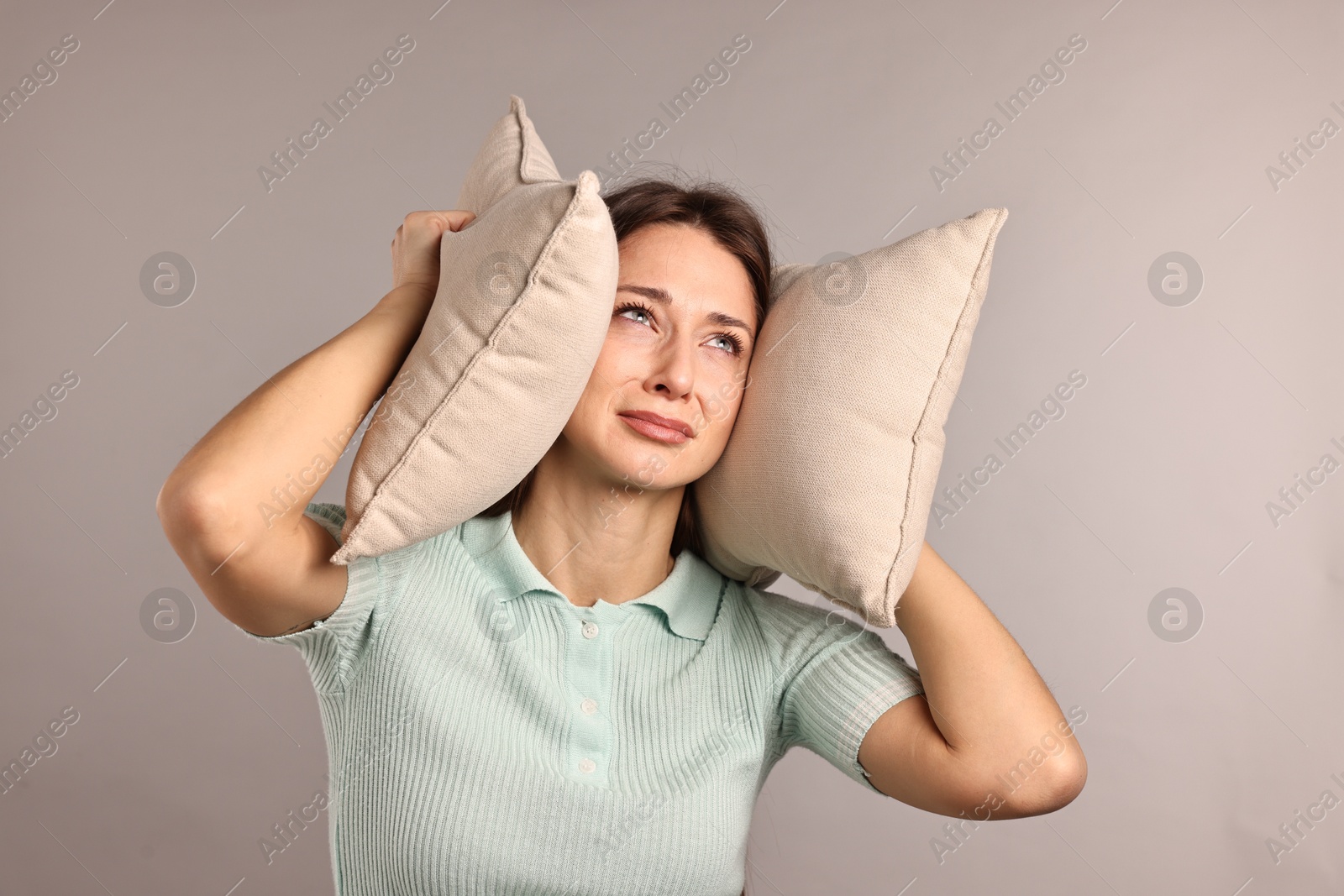 Photo of Annoyed woman covering her ears with pillows due to loud sound on light grey background