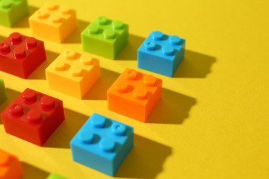 Photo of Construction toy. Colorful building bricks on yellow background, closeup