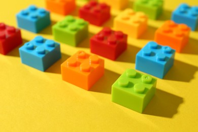 Photo of Construction toy. Colorful building bricks on yellow background, closeup