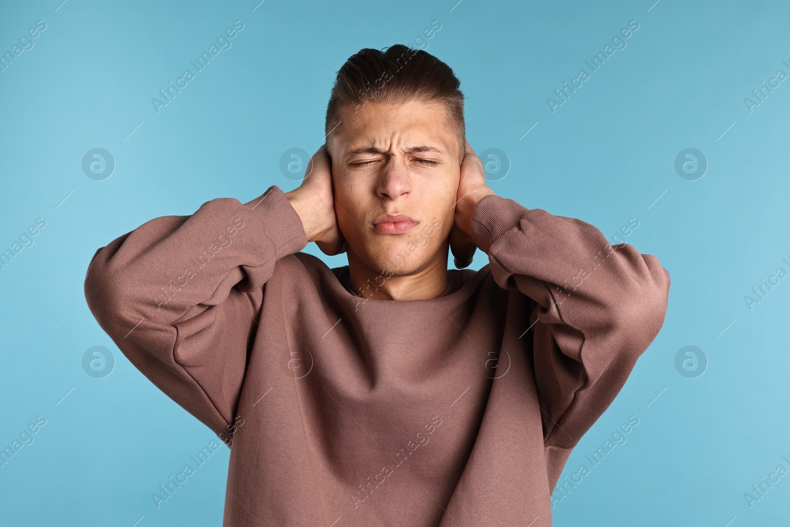 Photo of Annoyed young man covering his ears due to loud sound on light blue background