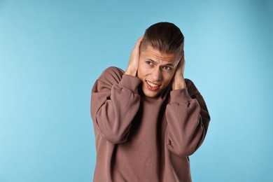 Photo of Annoyed young man covering his ears due to loud sound on light blue background