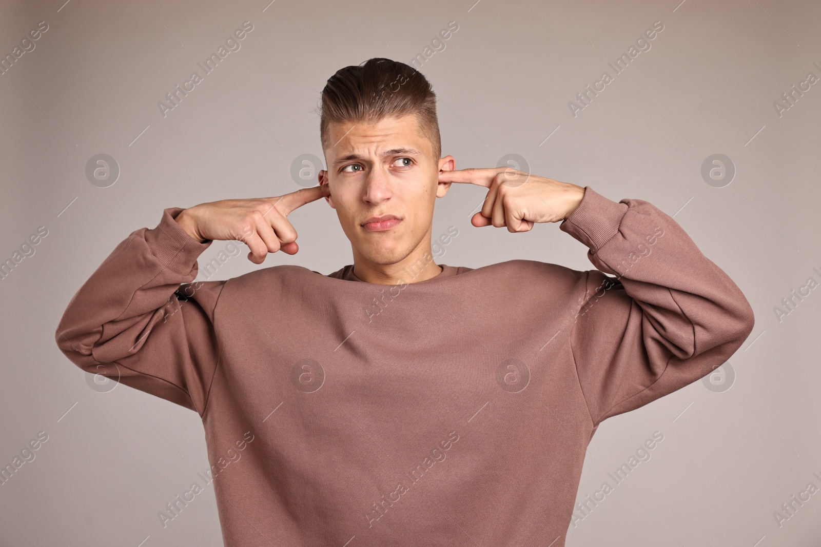 Photo of Annoyed young man covering his ears due to loud sound on light grey background