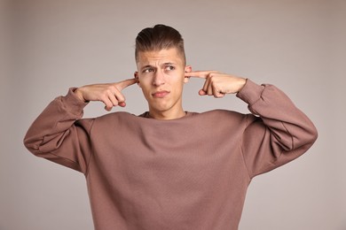 Annoyed young man covering his ears due to loud sound on light grey background