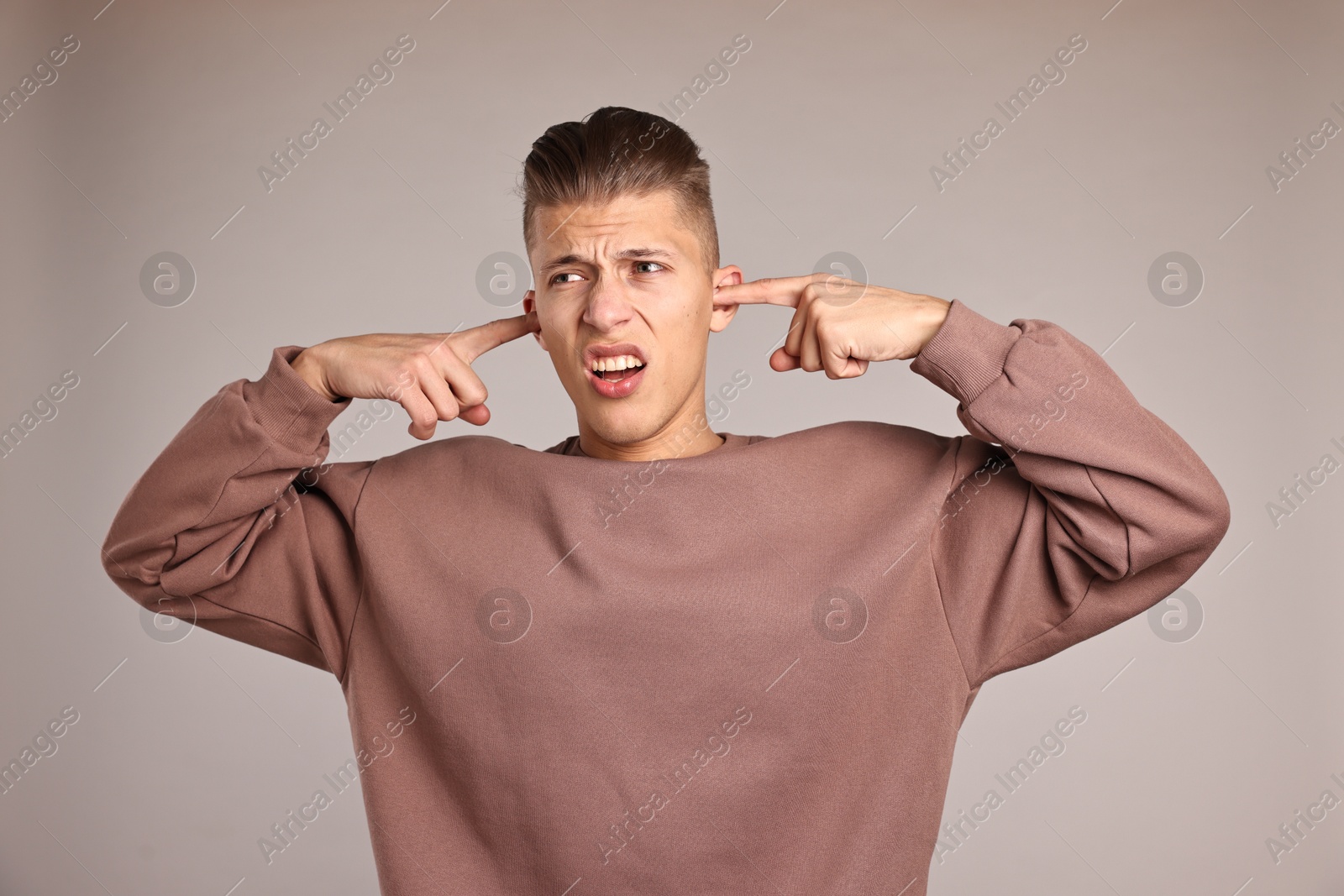 Photo of Annoyed young man covering his ears due to loud sound on light grey background