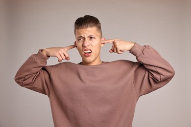 Annoyed young man covering his ears due to loud sound on light grey background