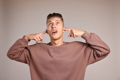 Photo of Annoyed young man covering his ears due to loud sound on light grey background