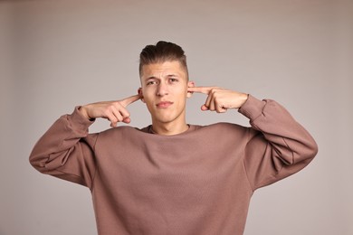 Annoyed young man covering his ears due to loud sound on light grey background