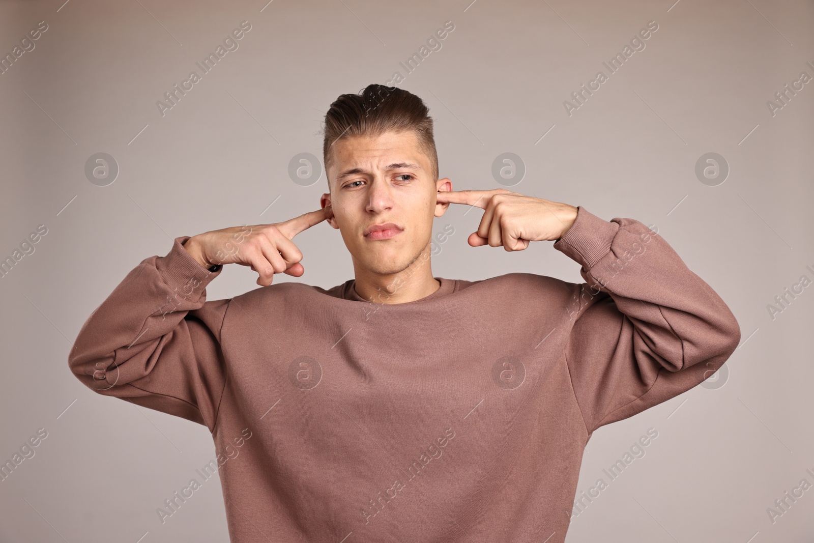 Photo of Annoyed young man covering his ears due to loud sound on light grey background