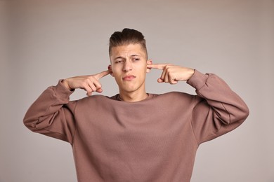 Photo of Annoyed young man covering his ears due to loud sound on light grey background