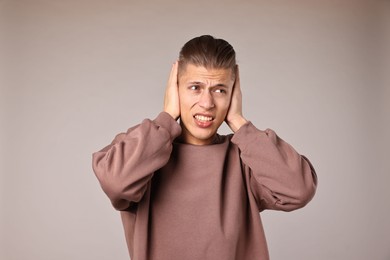 Photo of Annoyed young man covering his ears due to loud sound on light grey background