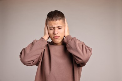 Photo of Annoyed young man covering his ears due to loud sound on light grey background