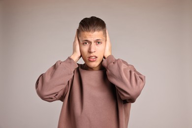 Photo of Annoyed young man covering his ears due to loud sound on light grey background