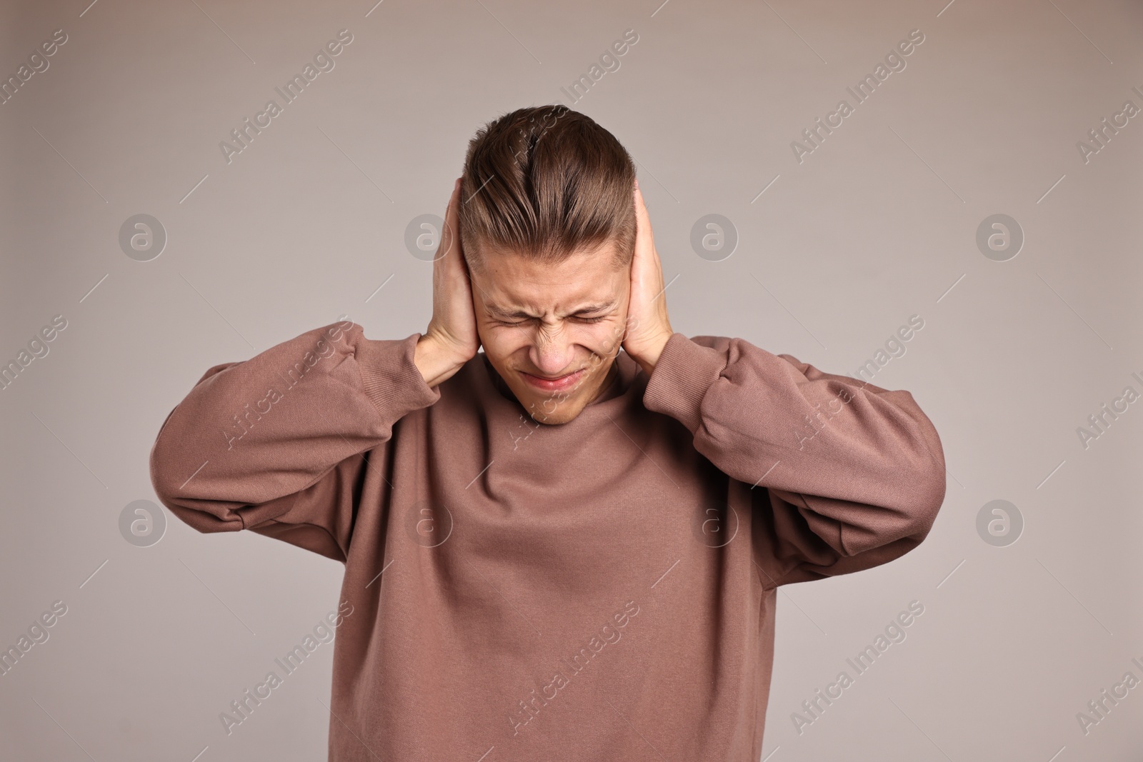 Photo of Annoyed young man covering his ears due to loud sound on light grey background